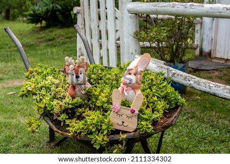 Rabbits sitting in a wheelbarrow full of flowers . Decorative flower bed.