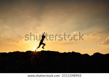Side shot of child jumping and running. She is happily running and playing outdoors. The background of the picture are sun and golden sky for copy space.