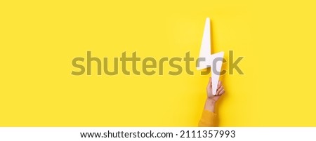 hand holding lightning bolt over yellow background, panoramic layout