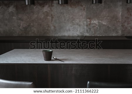 Beautiful coffee cup on island or table countertop in modern home kitchen. Dark grey kitchen design - detail of interior. Royalty-Free Stock Photo #2111366222