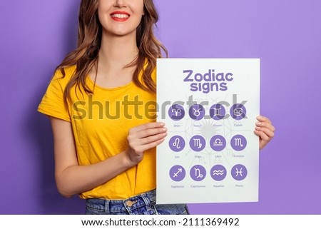 Young woman holding big paper poster with astrological icons of zodiac signs isolated on lilac background. School of Astrology