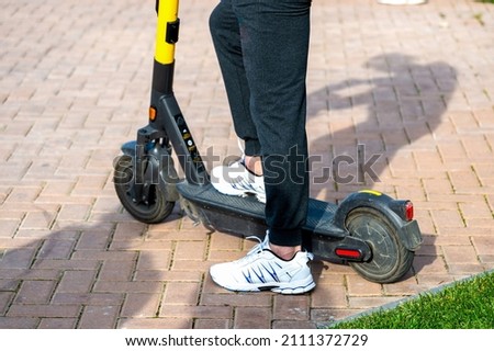 A man in sneakers and sweatpants in close-up, stepping on an electric scooter in a city park. Riding a scooter through the streets.  Royalty-Free Stock Photo #2111372729
