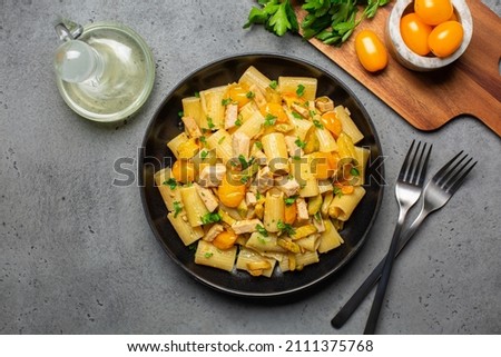 Paccheri Pasta With Swordfish, Cherry Yellow Tomato and zucchini in a black plate on a gray table. Directly above. Royalty-Free Stock Photo #2111375768