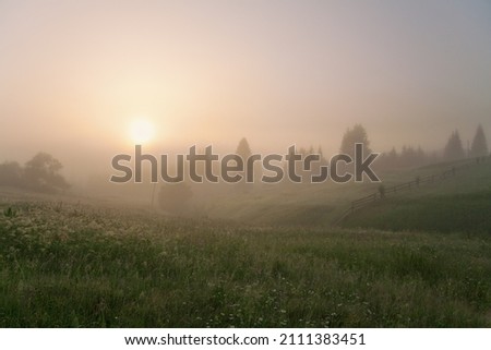 Sunrise over the mountain meadows, fog covers the sun and distant mountains. 