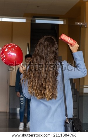 vertical portrait of girl waiting for her boyfriend in the doorway of her house to surprise him with a gift and a balloon to celebrate a special day. Valentine's Day, anniversary, birthday...