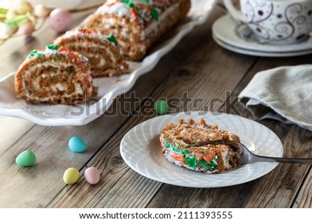 A serving of carrot cake jelly roll with a platter of the same in behind.