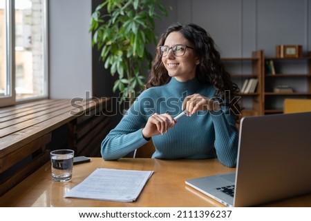 Positive happy female employee resting at workplace, looking away from computer screen. Relaxed woman office worker taking break to refresh mind and prevent stress during workday. Employee wellbeing Royalty-Free Stock Photo #2111396237