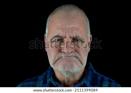 An old man looks angrily at the camera with his mouth pulled down. Royalty-Free Stock Photo #2111399084