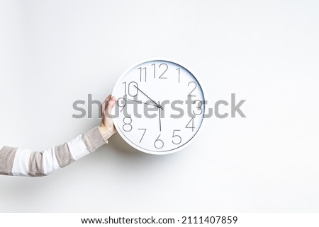 Woman's hand holds a large white clock against a light wall