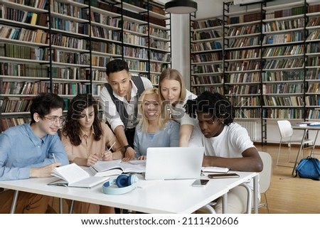 Multiracial group of teen gen Z students watching online learning presentation together, attending conference, webinar, writing notes, cooperating on research study in college library Royalty-Free Stock Photo #2111420606