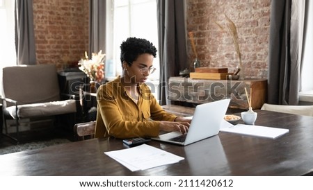 Focused millennial African owner woman using payment banking financial online app on laptop computer, working on domestic paper documents, paying bills, calculating taxes, insurance, mortgage fees