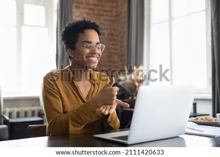 Smiling friendly African American therapist in glasses talking on video call, using sign language, speaking to patient with hearing disability, deafness, showing gestures at screen Royalty-Free Stock Photo #2111420633