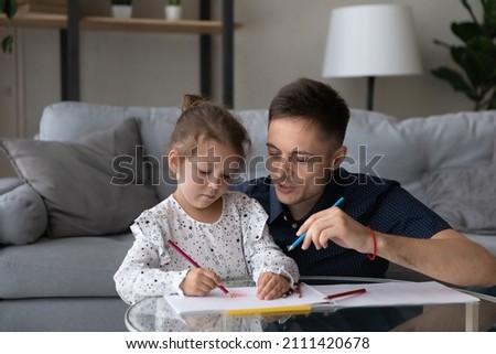 Focused adorable small child girl drawing in paper album with caring young father, spending leisure weekend time at home involved in domestic creative activity, early children development concept.