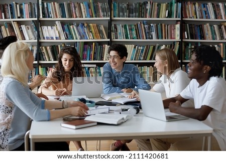 Happy diverse group of college students working together on study project in university library, sitting at table with books, laptop, talking discussing research, learning tasks, laughing Royalty-Free Stock Photo #2111420681