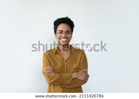 Cheerful confident African businesswoman wearing eyeglasses, posing with folded arms, looking at camera with toothy smile. Millennial female customer, young woman headshot portrait isolated on white Royalty-Free Stock Photo #2111420786