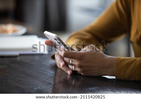 Hands of young dark skinned woman with finger rings using online app on mobile phone, making call, browsing Internet, chatting on social media, holding cellphone, texting, typing message. Close up Royalty-Free Stock Photo #2111420825