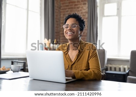Cheerful short haired African employee sitting at workplace with laptop in office, typing, looking at camera, smiling, laughing. Millennial worker, working business woman in casual head shot portrait Royalty-Free Stock Photo #2111420996