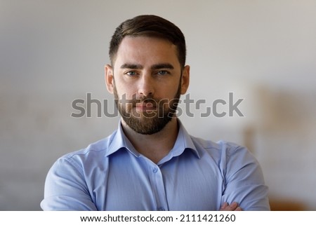 Confident serious millennial business man, successful company leader, founder, professional posing with hands folded, looking at camera. Businessman indoor head shot portrait