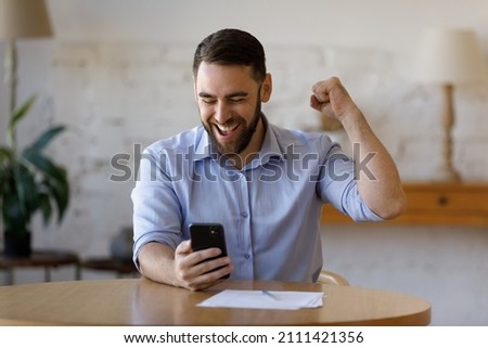 Happy excited smartphone user enjoying win, success, achieve, high job result. Euphoric businessman using cellphone, reading text message, feeling joy, making hand winner gesture, laughing Royalty-Free Stock Photo #2111421356