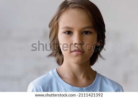 Serious pretty boy head shot portrait. Male school kid, schoolchild, young guy with neck-length brown hair looking at camera. Close up of face, front view. Childhood concept