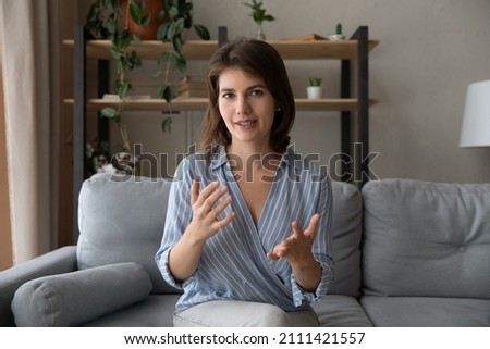 Focused beautiful young confident woman looking at camera, involved in video call conversation. Skilled female blogger streaming stories online in social network, female mentor sharing knowledge. Royalty-Free Stock Photo #2111421557