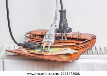 Electric power supply power cords cable plugged in open wallet placed on heating radiator battery at home. Payment of electricity and heating bills. Rising utility bills and expensive energy concept