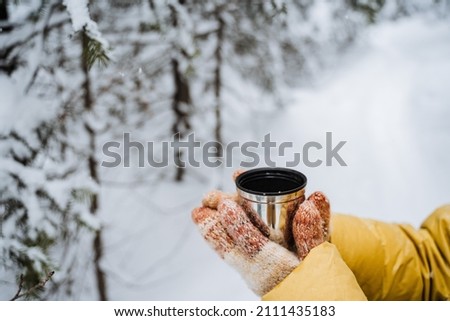 Thermo mug in hand. A hand holds a mug of hot tea. Drink tea in the winter outside. A metal cup with a drink is held by a person. Tea from a thermos. High quality photo