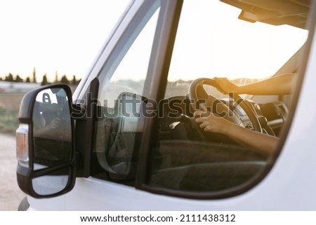 View from the outside of the steering wheel of a van and woman hands at sunset before starting the trip Royalty-Free Stock Photo #2111438312