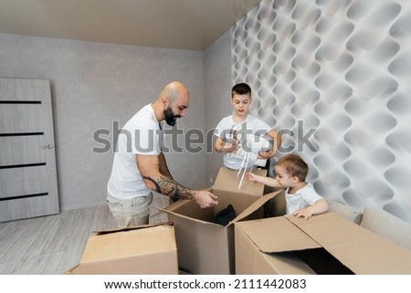 A young father with children unpacks a box of things after moving to a new apartment. Purchase of real estate. Housewarming, delivery and transportation of goods.
