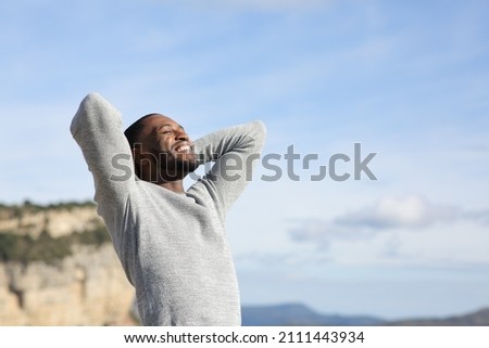 Relaxed man with black skin breathing fresh air with hands on head in the mountain Royalty-Free Stock Photo #2111443934