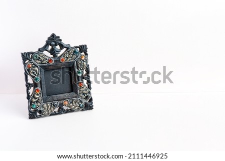 Photo frame vintage black carved from wood with colored pebbles in the interior. Pink background minimalism. 