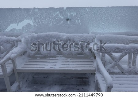 Summer white benches near a glass partition are covered with snow