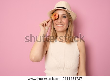 Portrait of a happy young woman wearing straw hat holding orange rose covering her eye