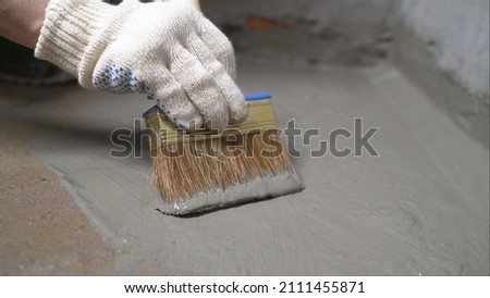 Workers cover the concrete screed with mortar and make waterproofing. The process of waterproofing the floor with a solution. Royalty-Free Stock Photo #2111455871