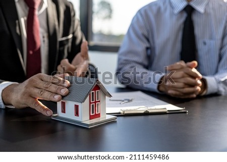 The property salesman on the project is pointing to a model of a small house to describe the structure and materials in the construction. Concept of selling housing estates and real estate.