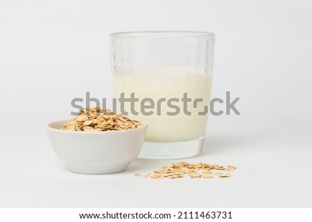 Oats as popular ingredient for variant of vegetable milk. Dry, raw oat flakes in bowl and milk in a glass ingredients for making oatmeal porridge on  white background  Royalty-Free Stock Photo #2111463731