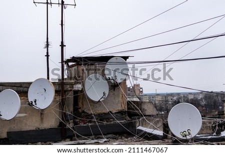 Satellite and TV antennas with numerous wires on roof of house on background of cityscape Royalty-Free Stock Photo #2111467067