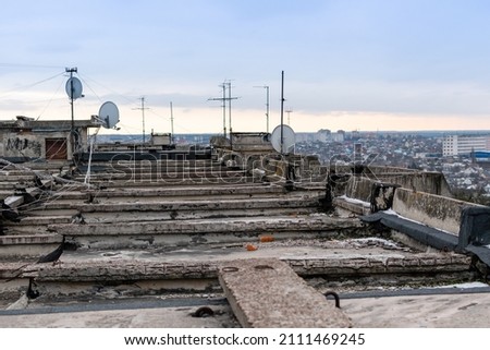 Roof of multi-storey building with old concrete structures and numerous TV antennas with wires on background of cityscape Royalty-Free Stock Photo #2111469245