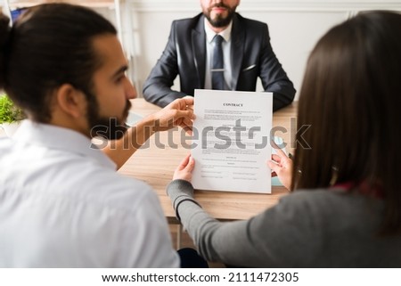 Rear view of an hispanic couple reading the contract and signing a business agreement with a finance consultant  