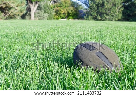 Old abandoned american football ball at field alone laying in green grass in park. Outdoors sports concept. Horizontal summer background photo with copy space. Active lifestyle. Design template.