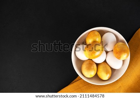 Yellow Easter eggs in a bowl on a dark background. Natural duing Easter eggs with turmeric powder in yellow color.