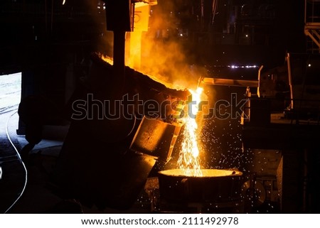 Molten metal pours from metallurgy ladle. Smoke, black background.