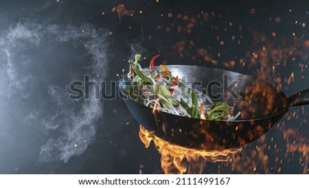 Freeze Motion of Wok Pan with Flying Ingredients in the Air and Fire Flames. Royalty-Free Stock Photo #2111499167