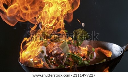 Freeze Motion of Wok Pan with Flying Ingredients in the Air and Fire Flames. Royalty-Free Stock Photo #2111499227