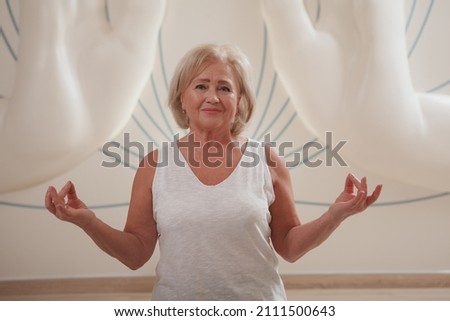 Lovely senior woman smiling doing hand mudras while meditating