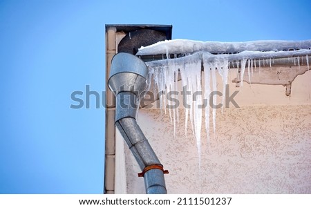 Sharp icicles hanging down from roof of the building. Icicles on facade of building, dangerous icicles melt on rooftop, risk of injury. Melting icicle danger for pedestrians Royalty-Free Stock Photo #2111501237