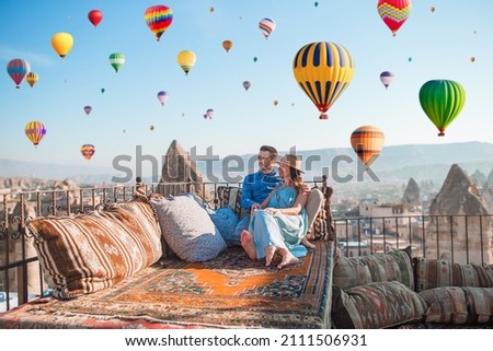 Young couple at sunrise on a rooftop in Cappadocia with hot air balloons in the background. Couple travels the world. Hot air balloon flights. Royalty-Free Stock Photo #2111506931