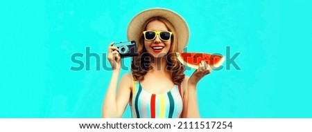 Summer portrait of happy laughing young woman with retro film camera and slice of fresh watermelon wearing straw hat on blue background
