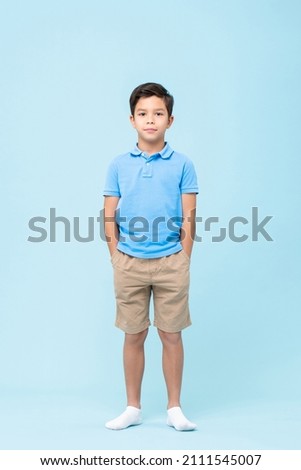 Full body self assured child in casual clothes and socks holding hands in pockets and looking at camera against blue background Royalty-Free Stock Photo #2111545007
