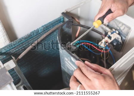 A technician dismantles the inside of a outdoor compressor unit of a Split type air conditioner. Repair or maintenance work. Royalty-Free Stock Photo #2111555267